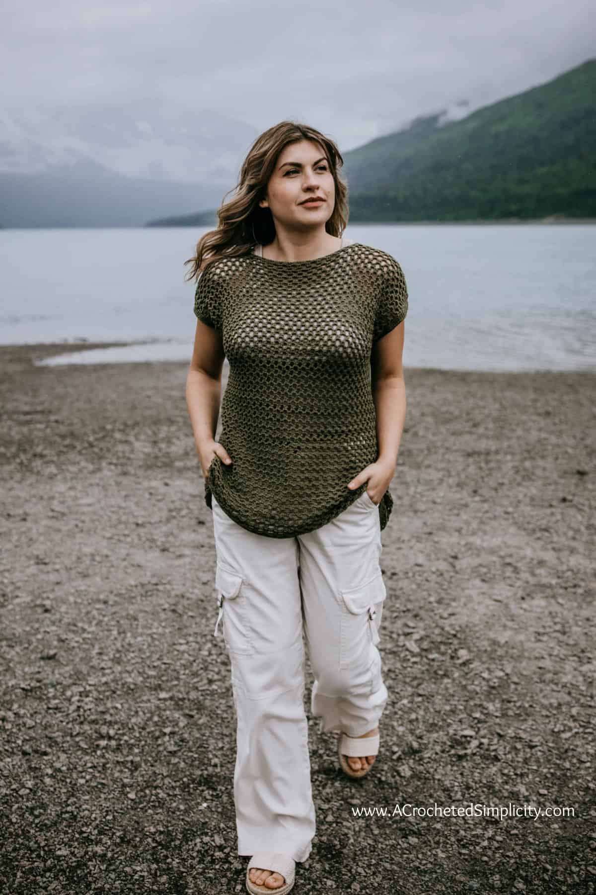 Model walking on the beach with hands in pockets wearing a summer crochet top pattern.