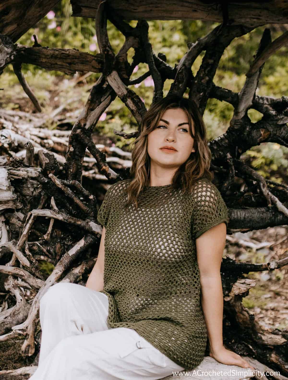 Model wearing honeycomb crochet mesh top sitting on driftwood.