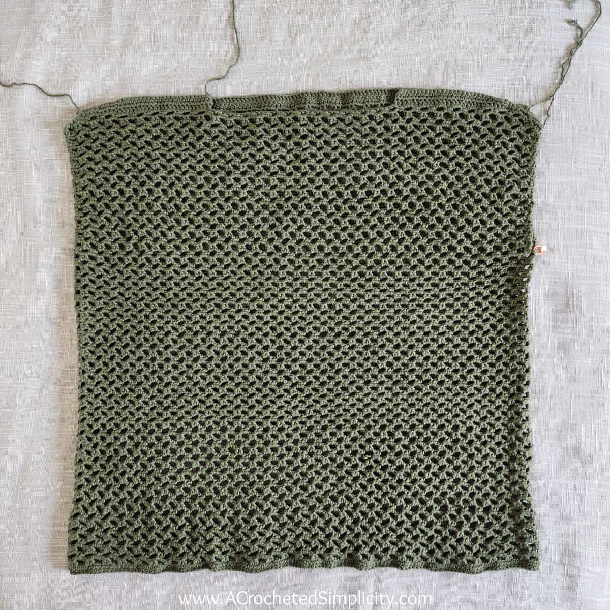 Olive green mesh crochet top laying on ecru fabric.