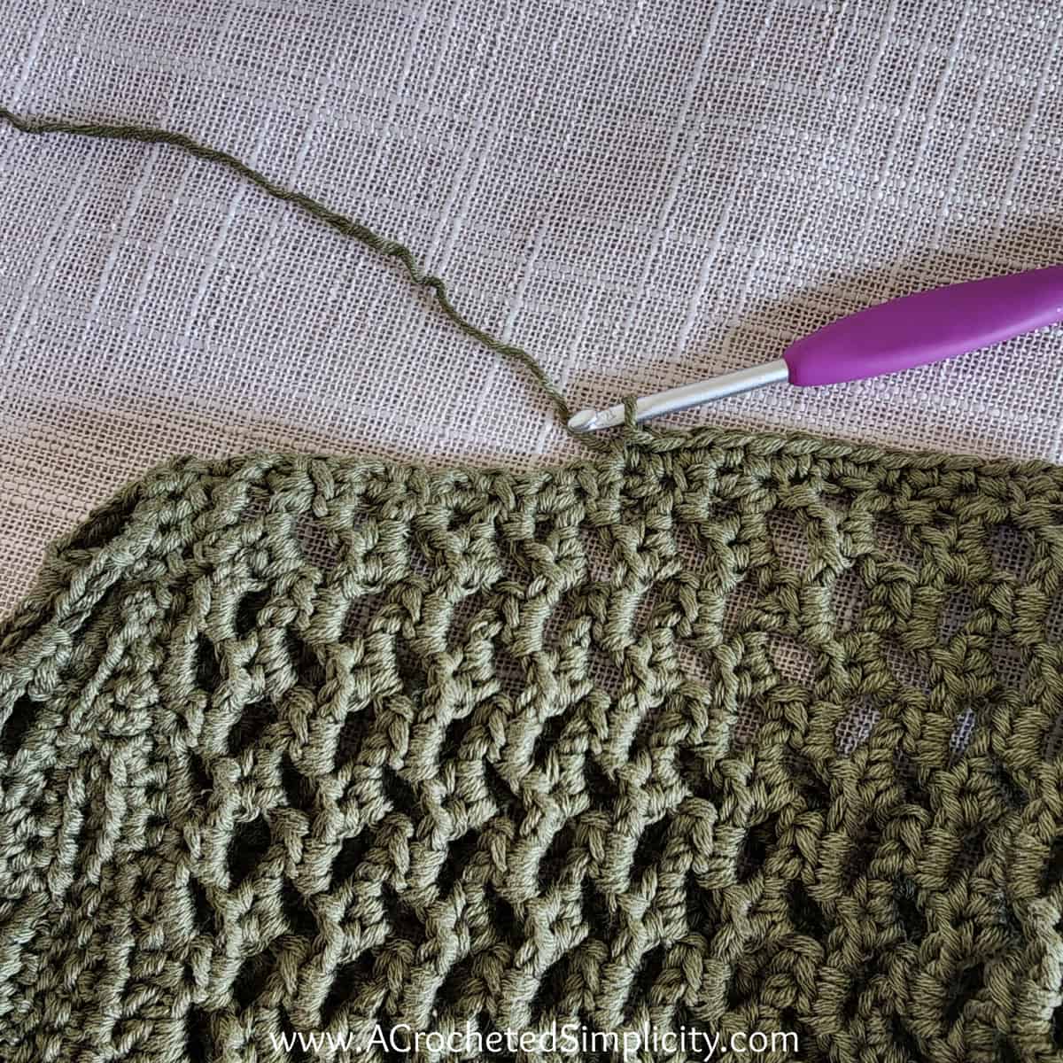 Purple crochet hook edging the armhole opening of a mesh crochet top.