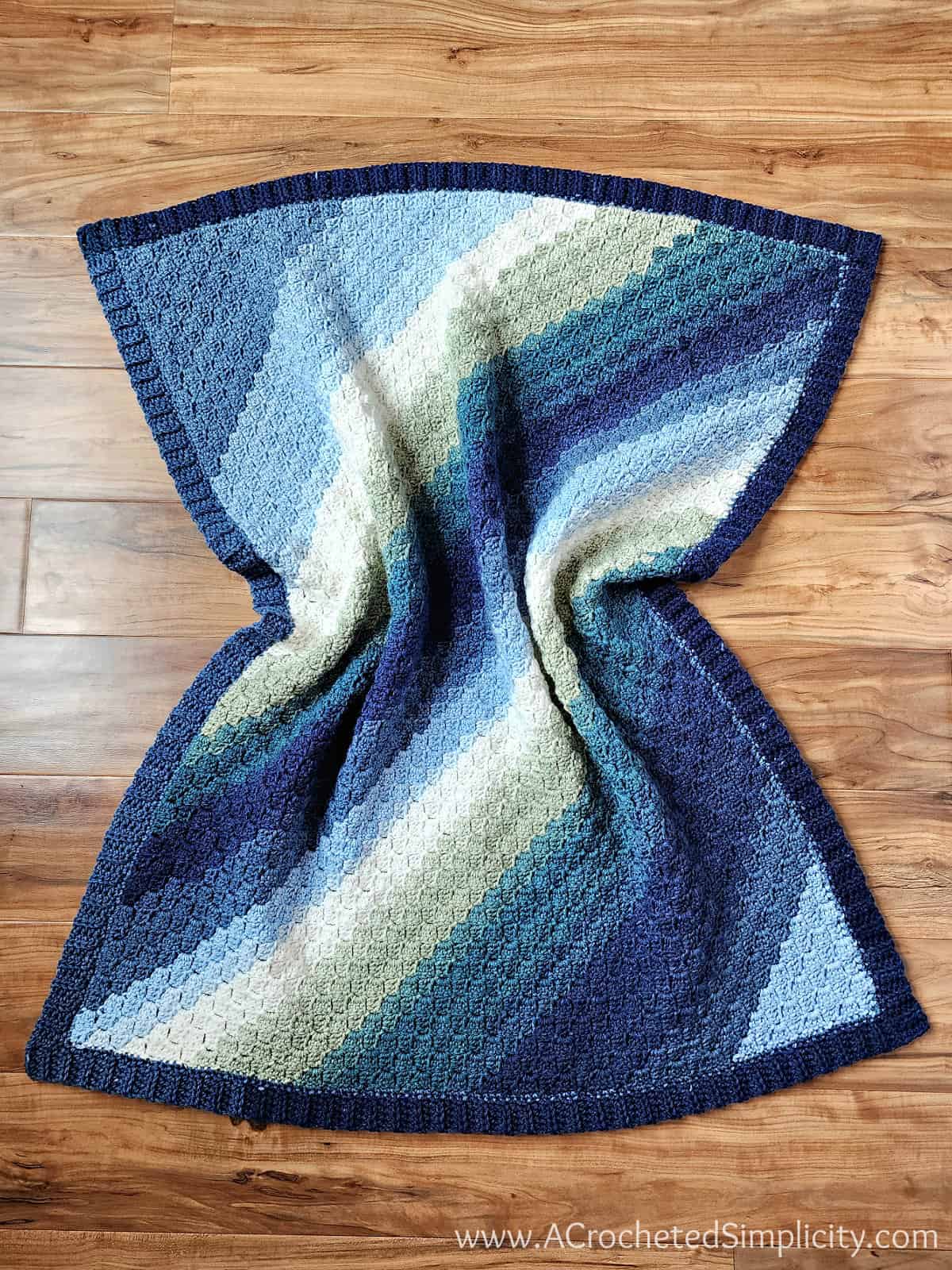 Crochet C2C baby blanket in blue ombre yarn laying on a wood floor.