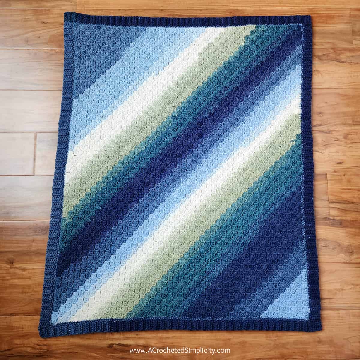 Crochet C2C rectangle baby blanket in blue ombre yarn laying on a wood floor.