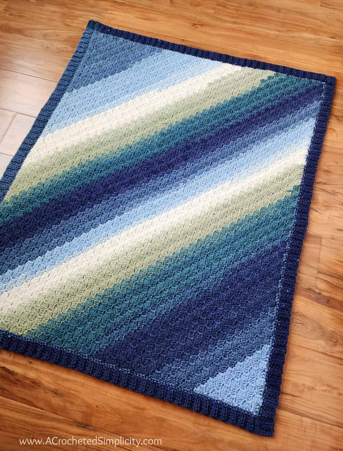 C2C crochet rectangle baby blanket in Mandala Baby yarn laying on a wood floor.