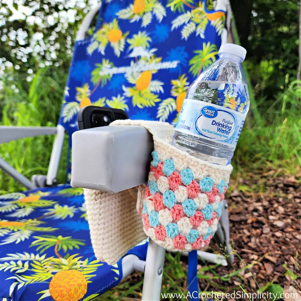 Granny stitch crochet chair caddy hanging on beach chair with water and phone.