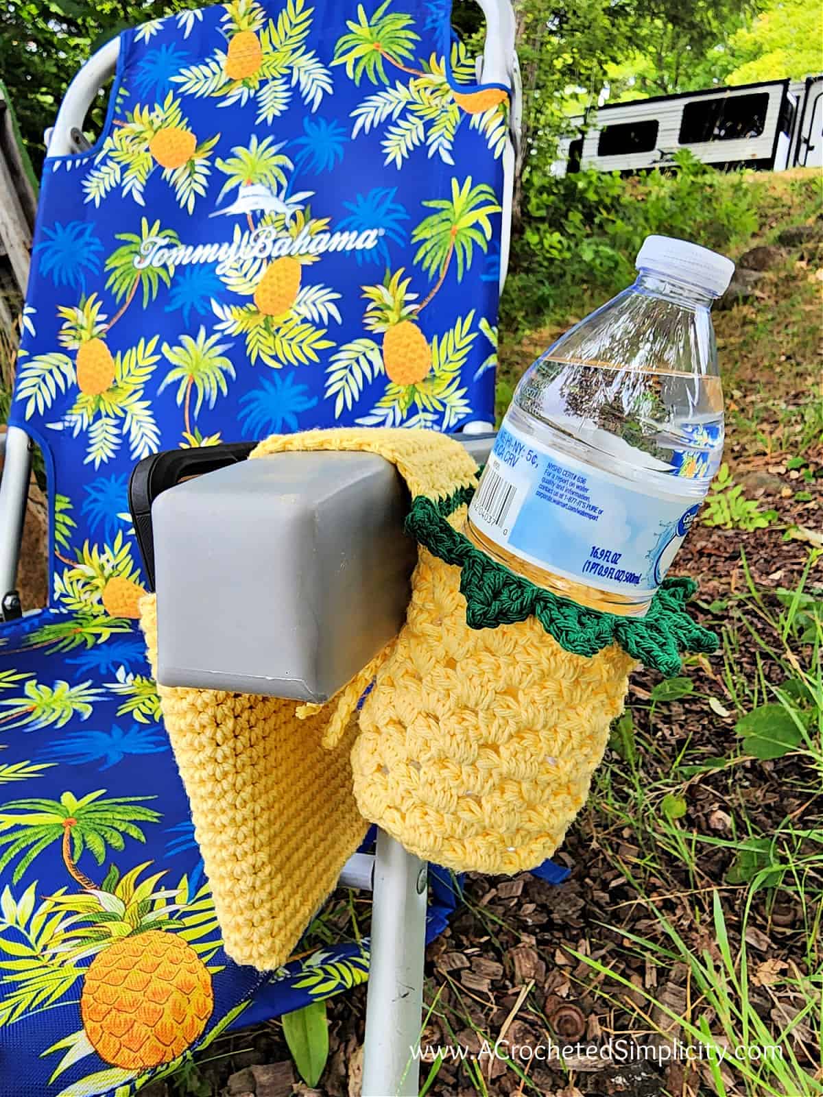Pineapple crochet chair caddy hanging on beach chair with water and phone.