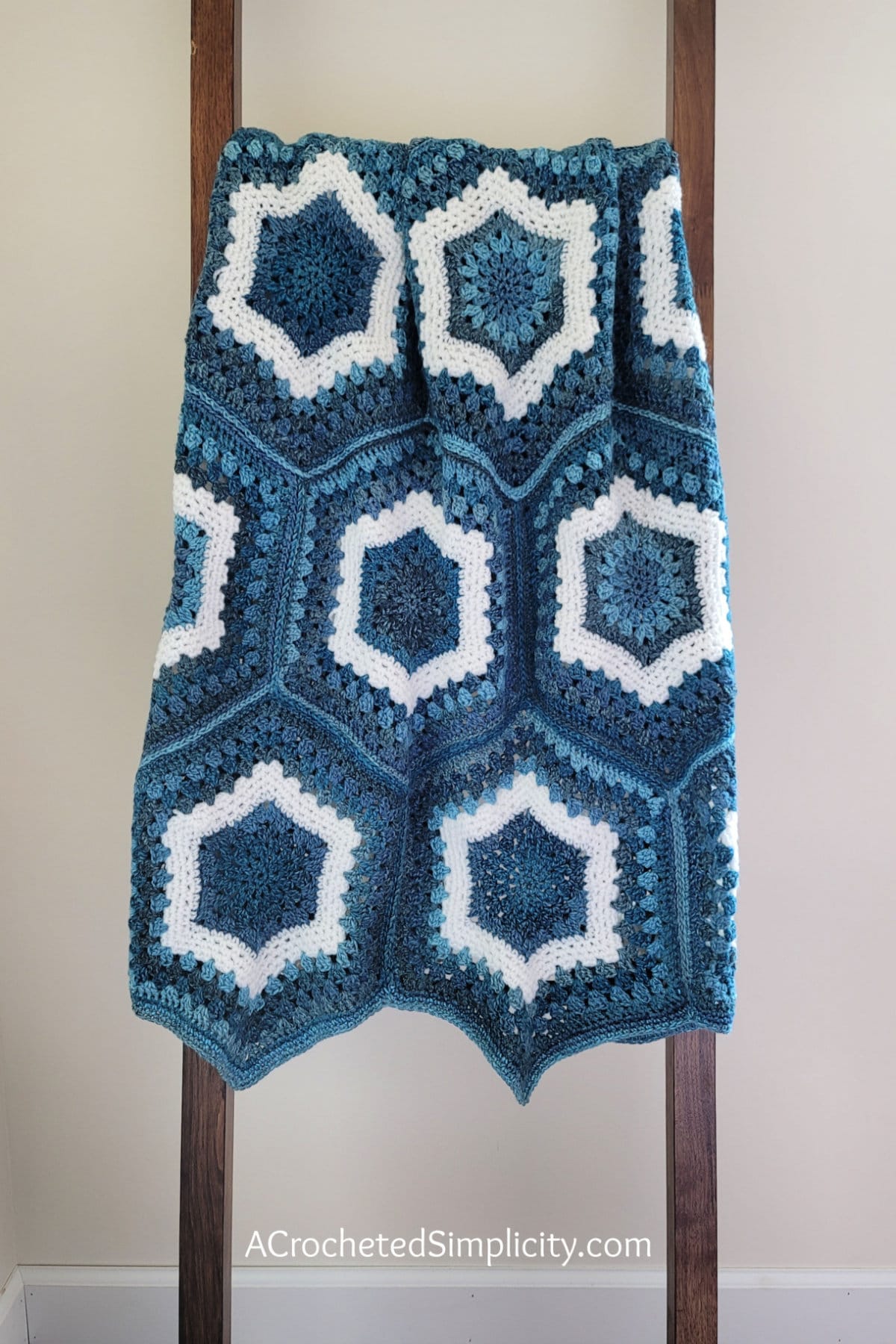 Crochet hexagon blanket in shades of blue and white yarn hanging on wood blanket ladder.