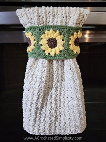 Sunflower crochet dish towel hanging on oven door handle.