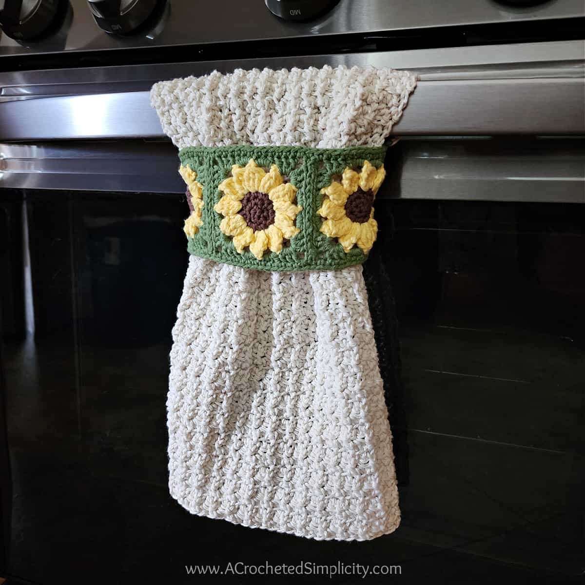 Sunflower motif crochet kitchen towel hanging on oven door.