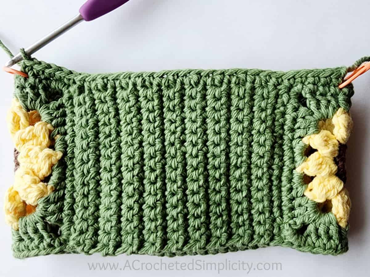 A purple crochet hook was used to crochet a row of single crochet along one edge of the sunflower motifs.