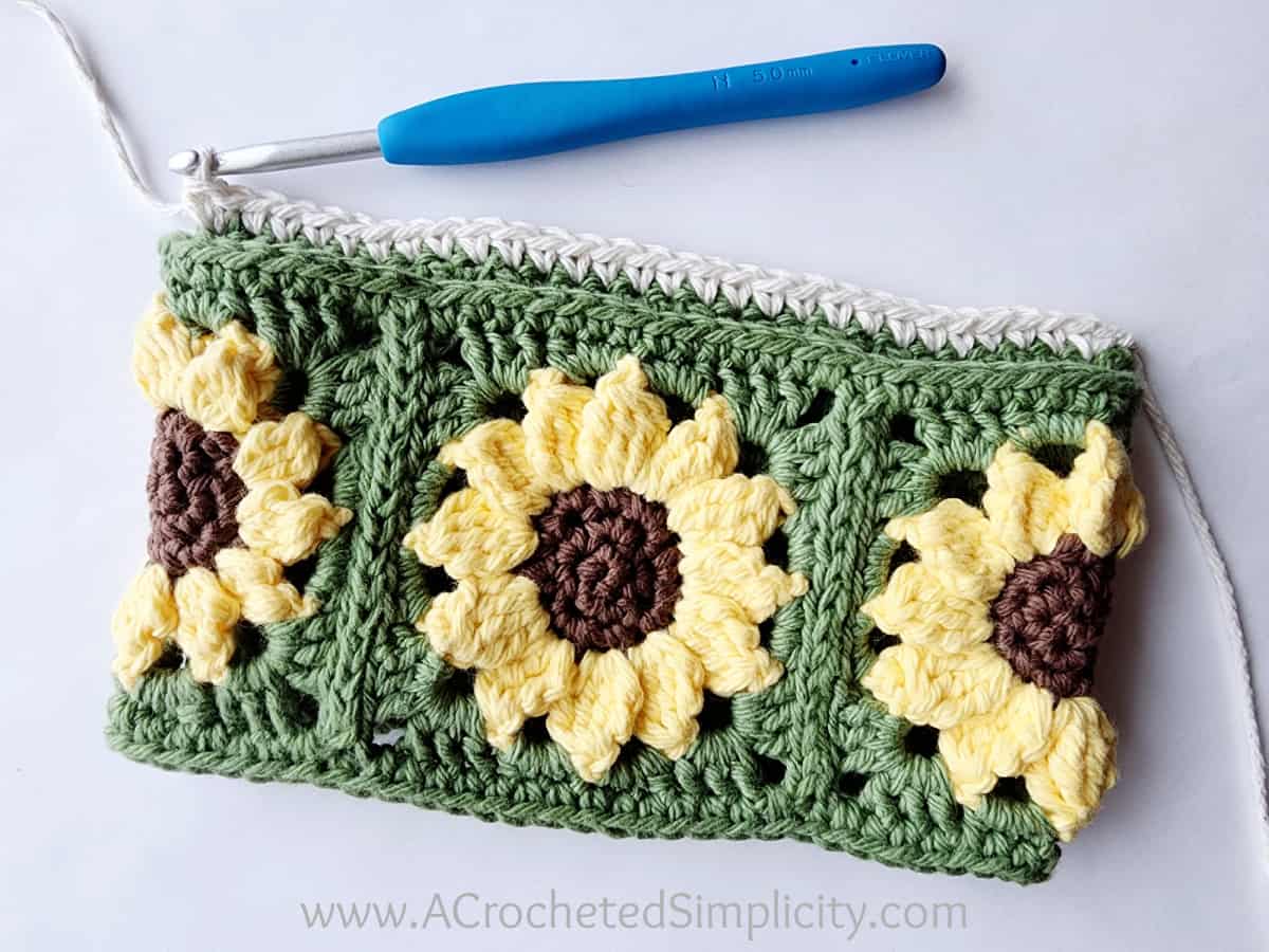 Green and yellow sunflower squares that form a loop and ecru yarn has been added to begin the towel.