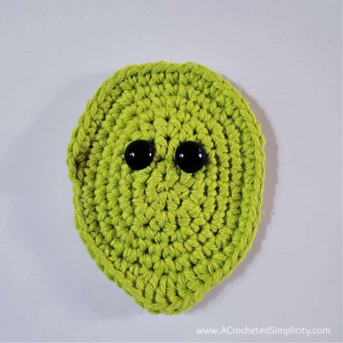 Crochet oval in green for small witch face with two black eyes.