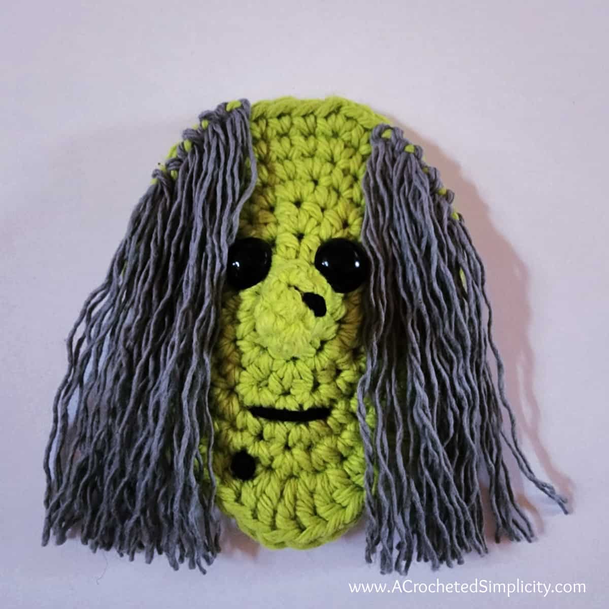 Crochet witch head finished with small smile and yarn wart on her chin.