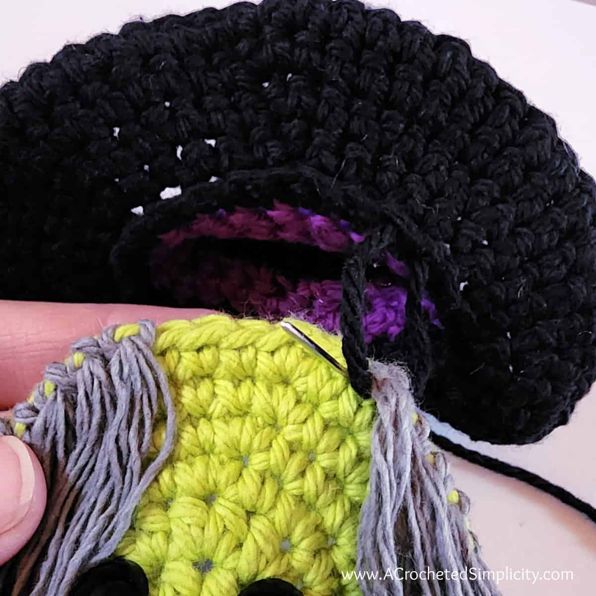 Yarn needle and tail of yarn attaching witch's hat to her head.
