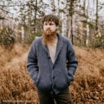 Man modeling a shawl collar crochet cardigan standing in the woods during the fall