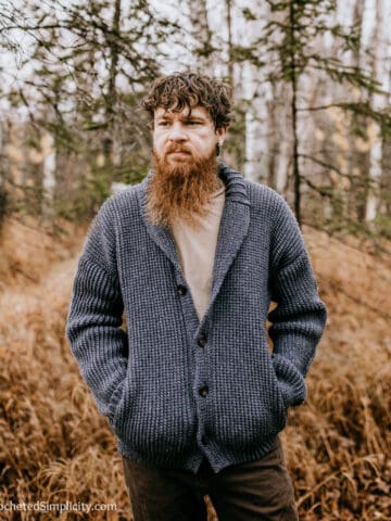 Man modeling a shawl collar crochet cardigan standing in the woods during the fall