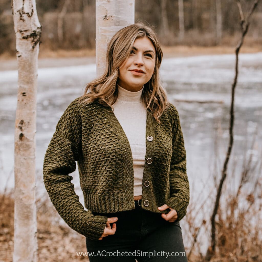 woman modeling olive green button up crochet cardigan leaning on birch tree