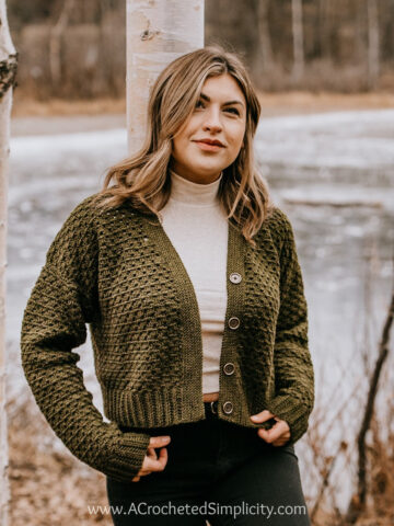 woman modeling olive green button up crochet cardigan leaning on birch tree