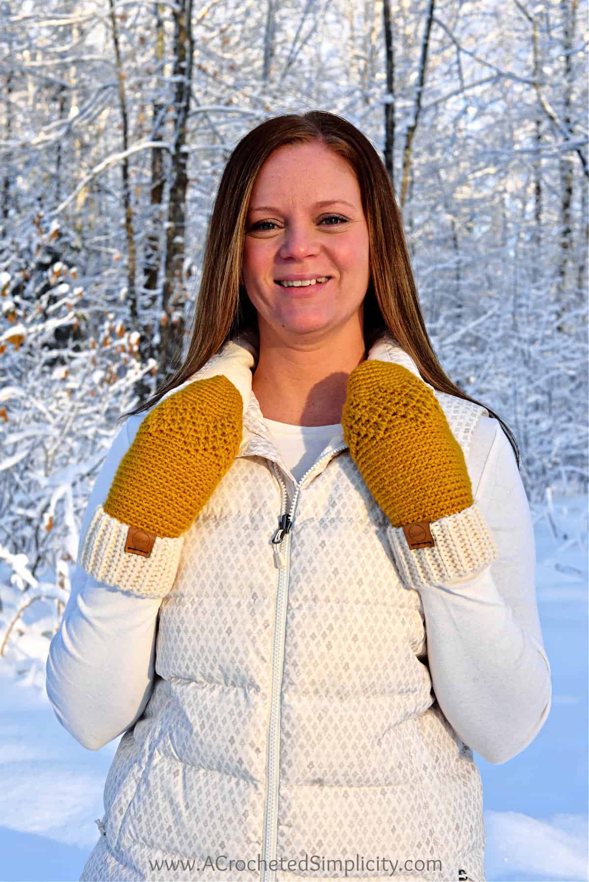 woman modeling mitten crochet pattern in gold wearing cream vest outside in snowy winter