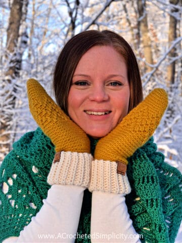 close up of woman holding crochet mittens on her face