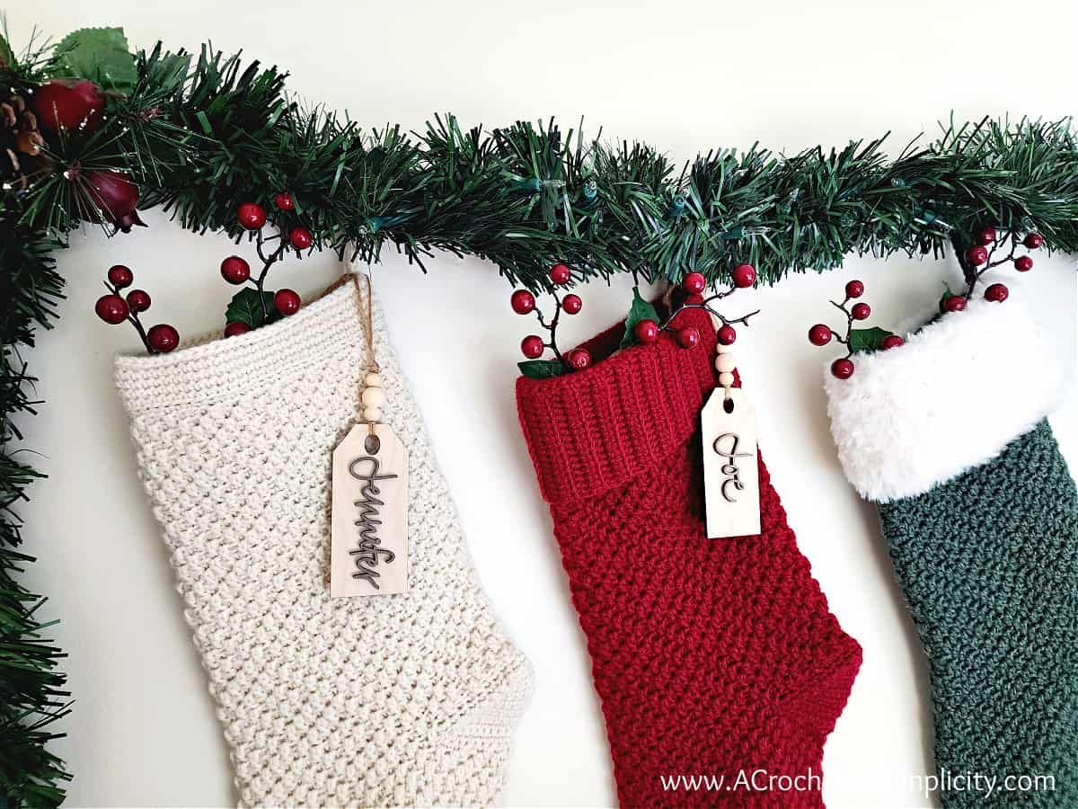 three crochet stockings hanging with garland and berries