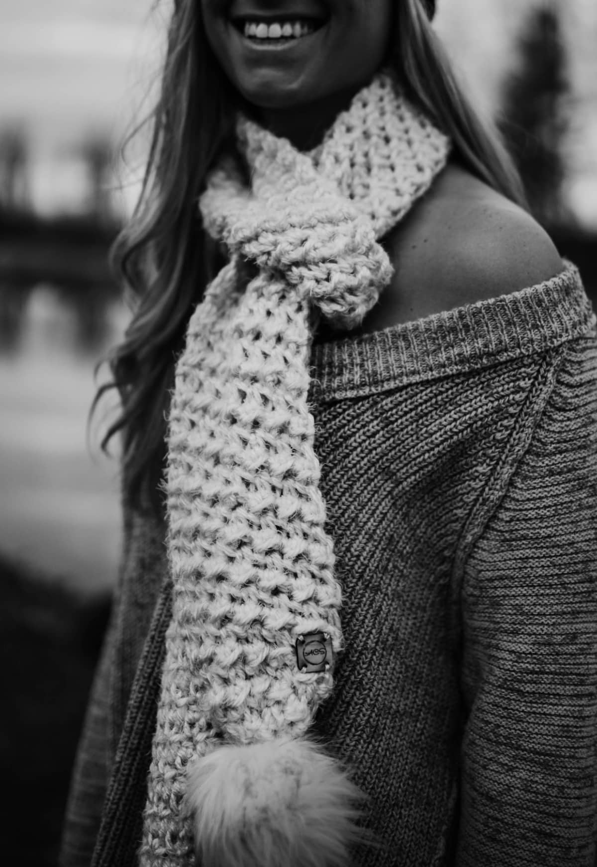 black and white close-up of woman modeling chunky crochet scarf in cream with faux fur poms