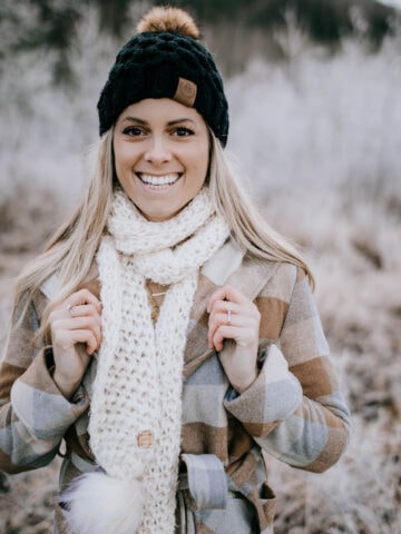 Woman modeling chunky crochet scarf in cream with faux fur poms