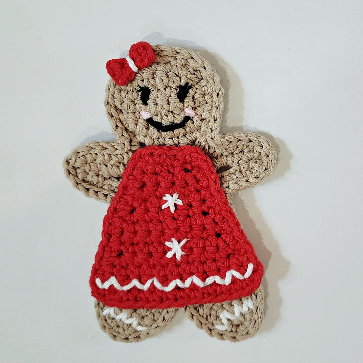 Crochet gingerbread girl wearing red dress with red hair bow.