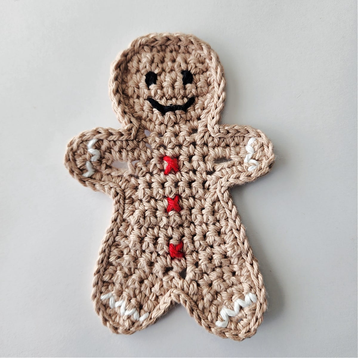 crochet gingerbread man ornament with red buttons, white ric rac trim, and black crochet eyes and mouth