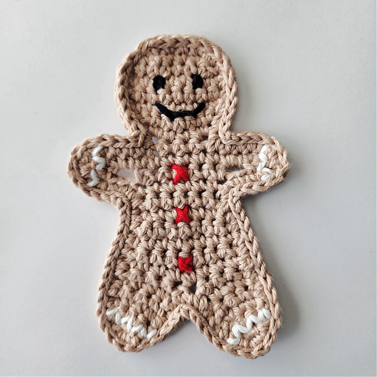 crochet gingerbread boy with red buttons, white ric rac trim, and black crochet eyes and mouth