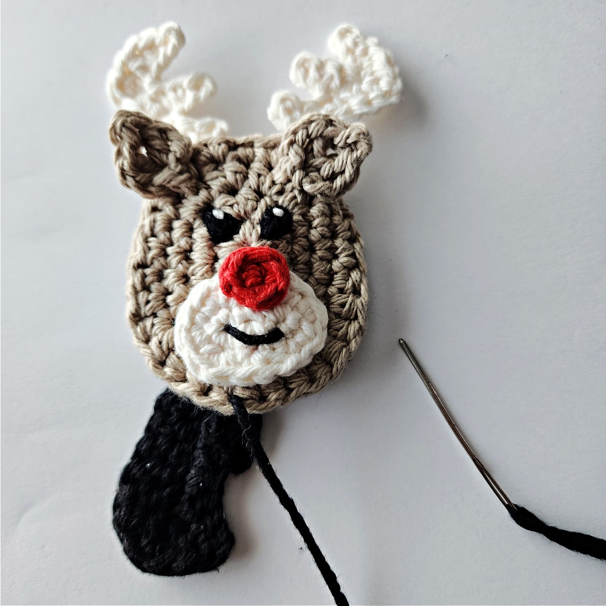 Yarn needle and black yarning attaching hooves onto the reindeer.