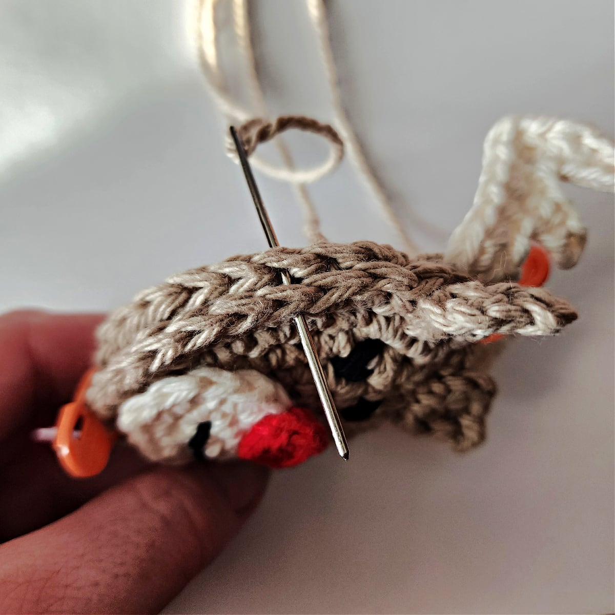 Yarn needle being inserted through both layers of the crochet reindeer's heads.