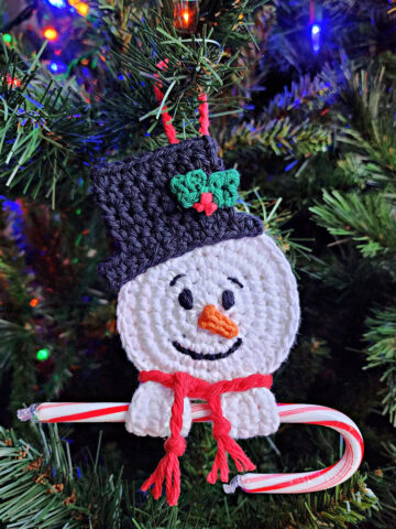 crochet snowman candy cane holder ornament hanging on christmas tree with candy cane