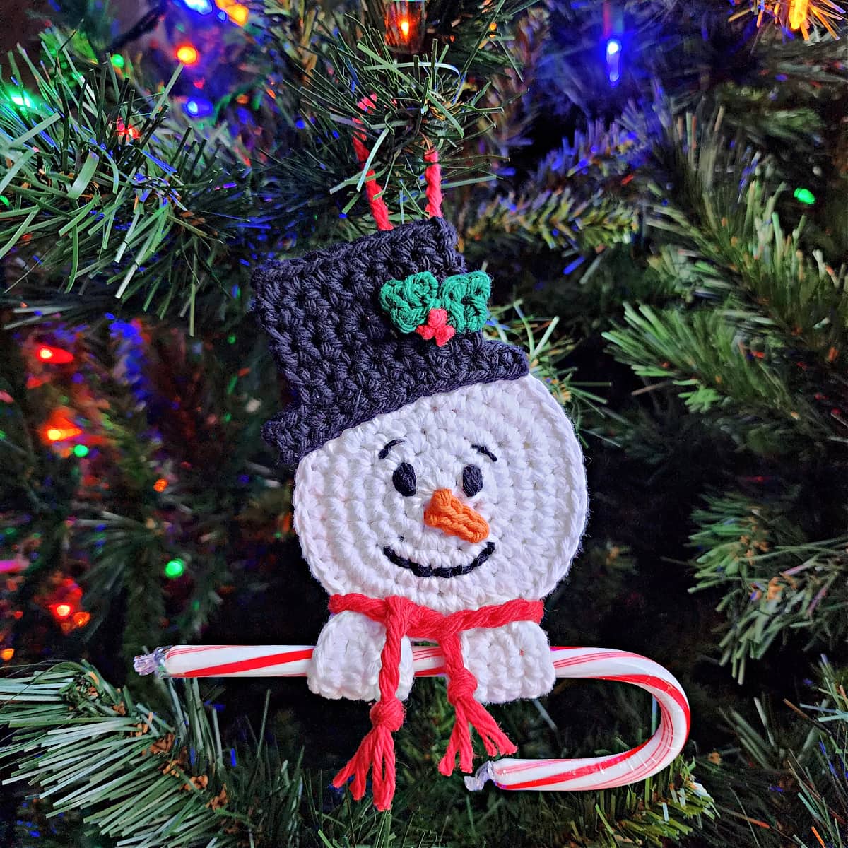 crochet snowman candy cane holder ornament hanging on christmas tree with candy cane