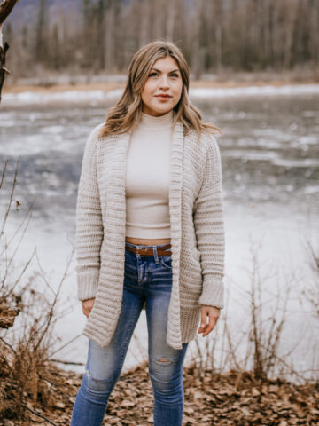 Woman modeling long crochet cardigan with pockets outside in woods.