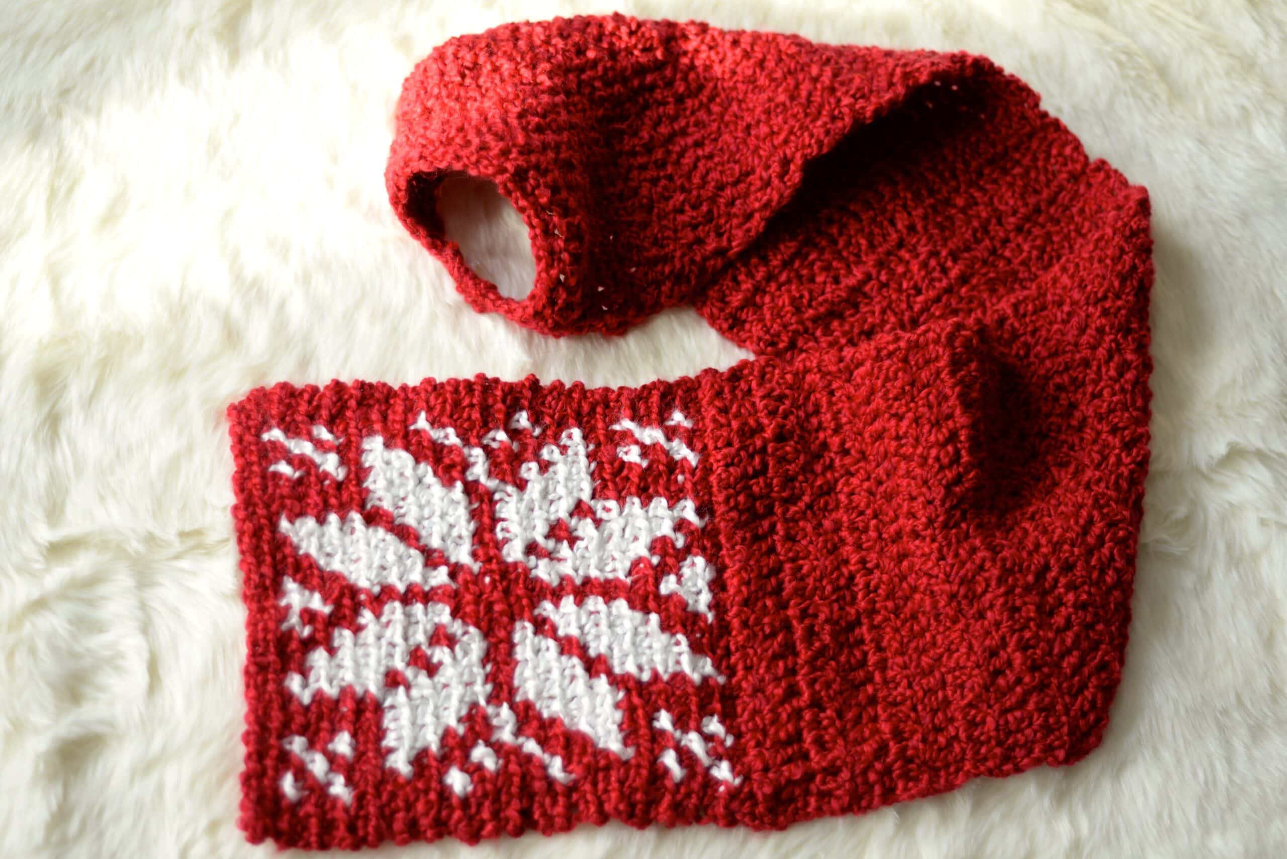 red crochet keyhole scarf with white snowflake laying on fur