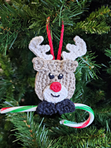 crochet reindeer candy cane holder ornament hanging on christmas tree with candy cane
