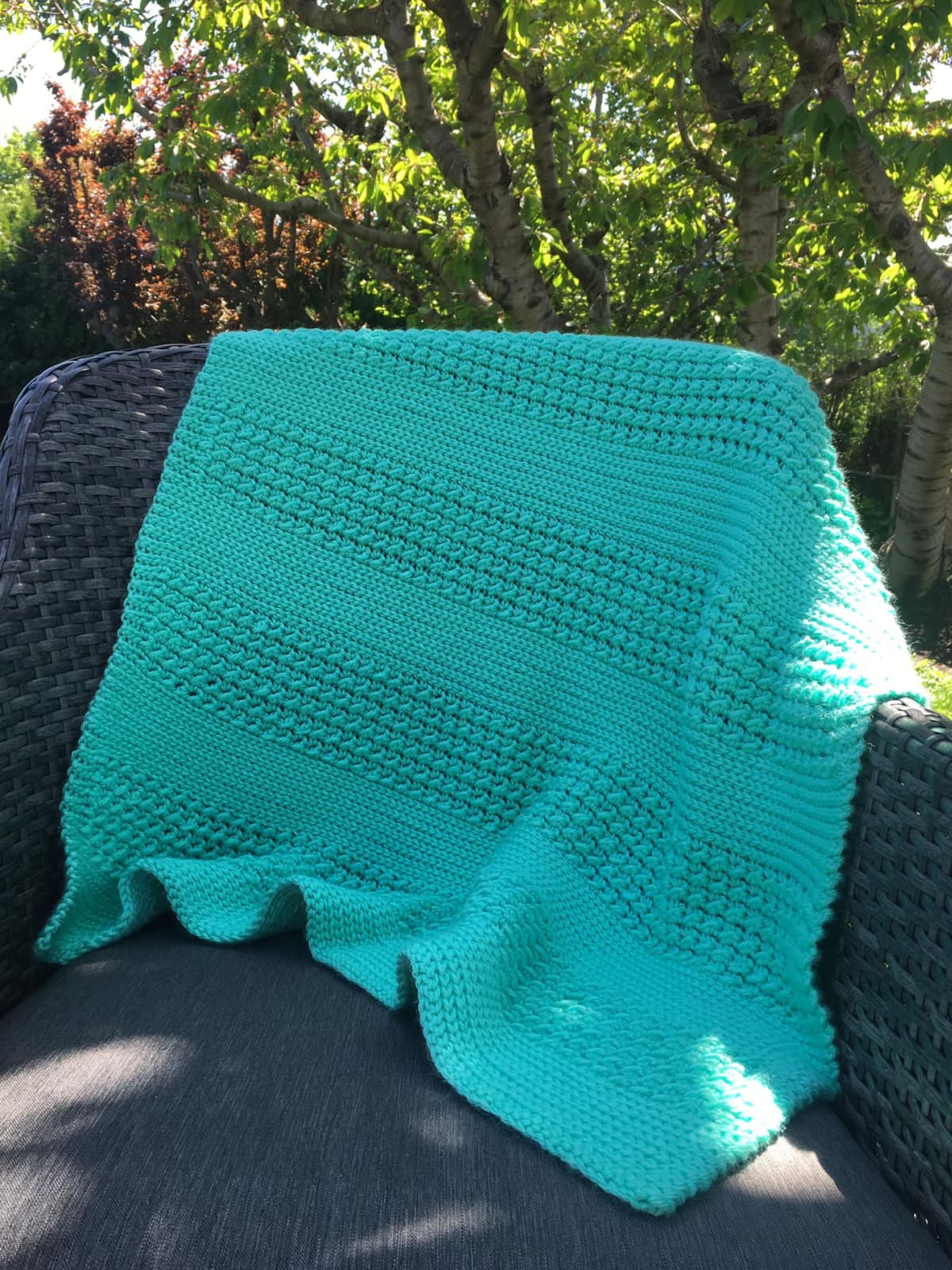 Crochet baby blanket in green draped over a dark chair sitting outside.