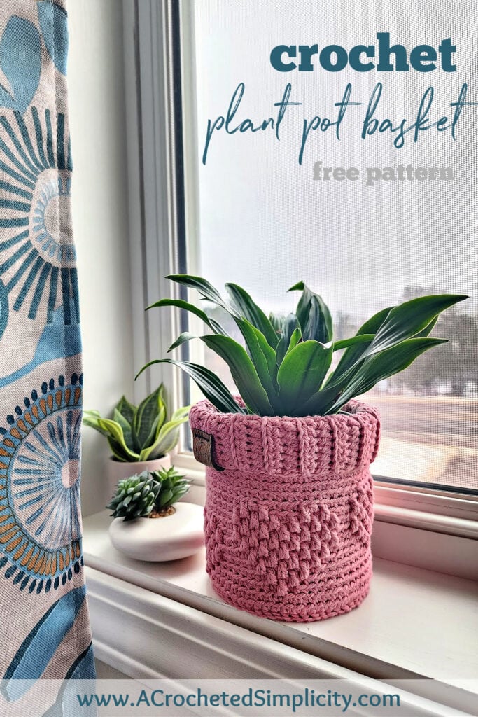 Pink crochet flower basket with small embossed heart pattern sitting in a windowsill in the sun.