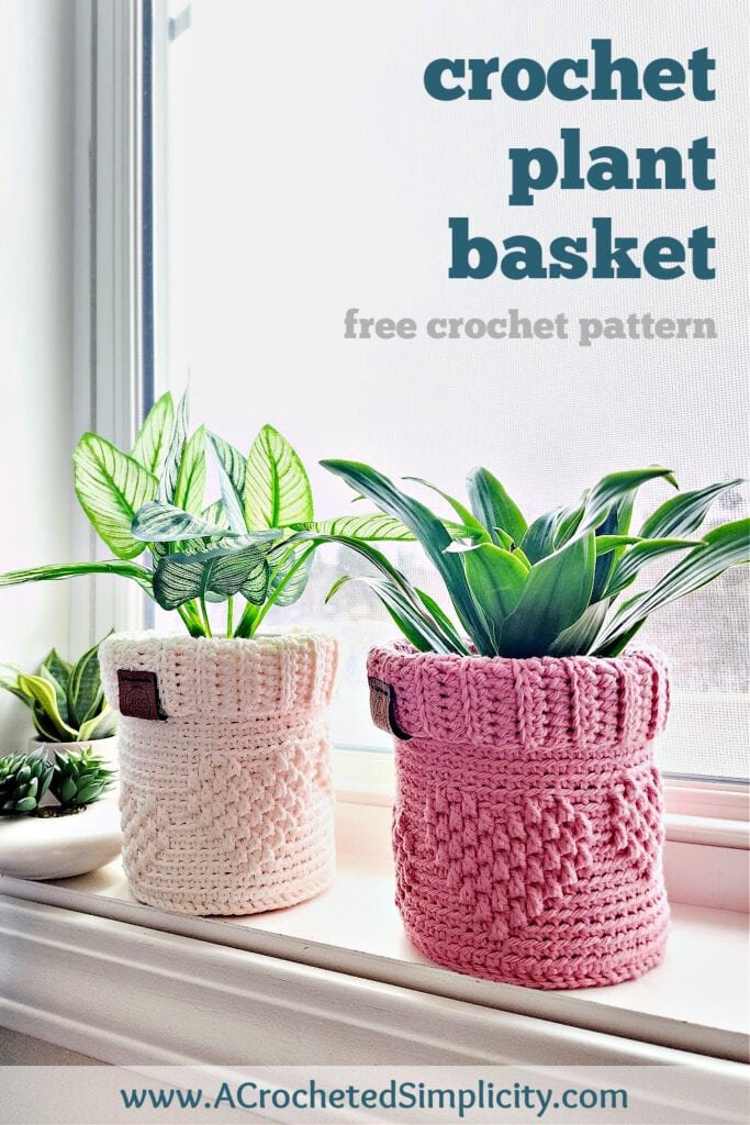 Two crochet plant pot covers sitting on a windowsill in the sun with indoor houseplants.