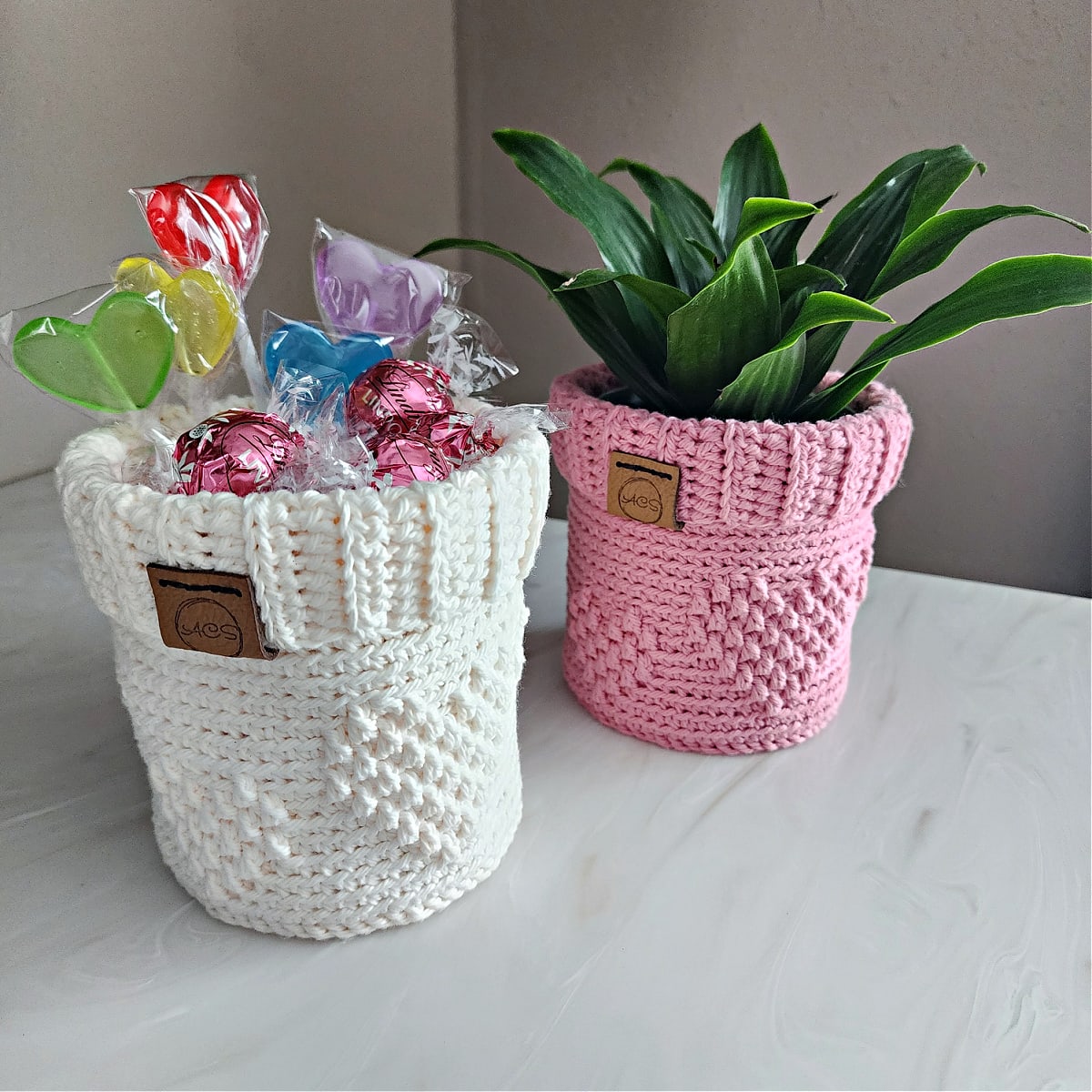 Pink crochet plant pot cover with an indoor house plant and cream color crochet candy dish filled with candy.