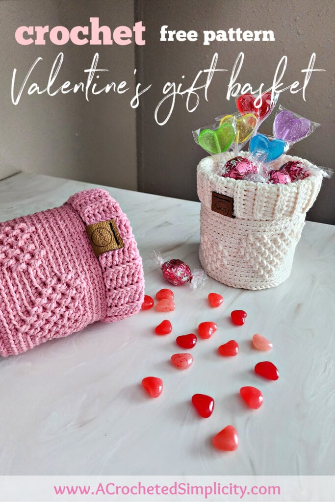 Pink crochet candy basket laying down with candy spilling out and a cream crochet gift basket next to it filled with candy.