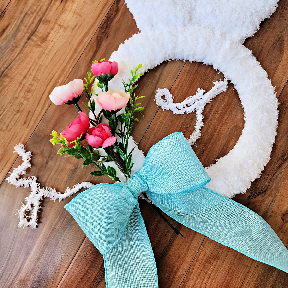 Wired blue ribbon bow laying on top of floral sprig to be attached to easter bunny wreath.