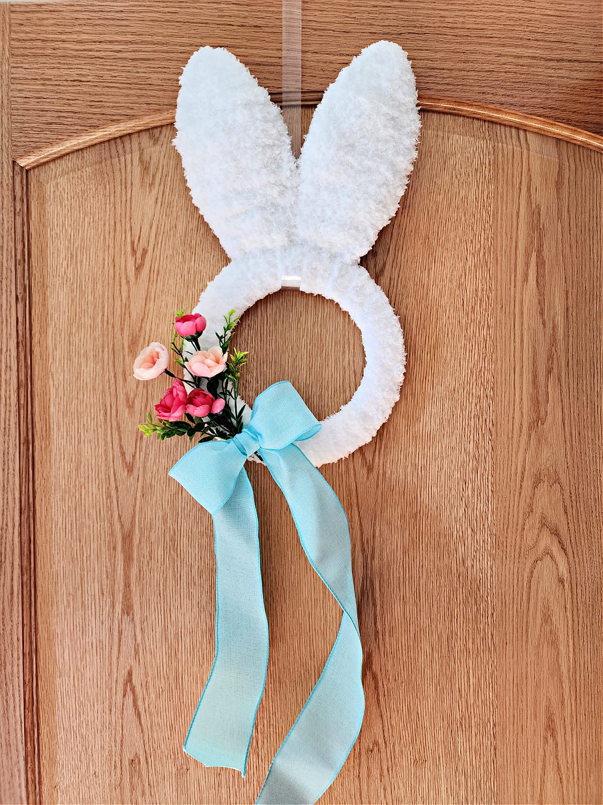Crochet bunny wreath with flowers and bow hanging on wood door.