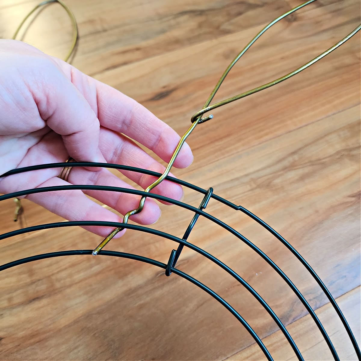 Coat hanger bunny ear being inserted through round wire wreath frame.