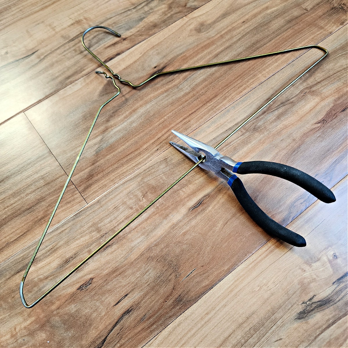 Needle nose pliers cutting long edge of coat hanger in half.