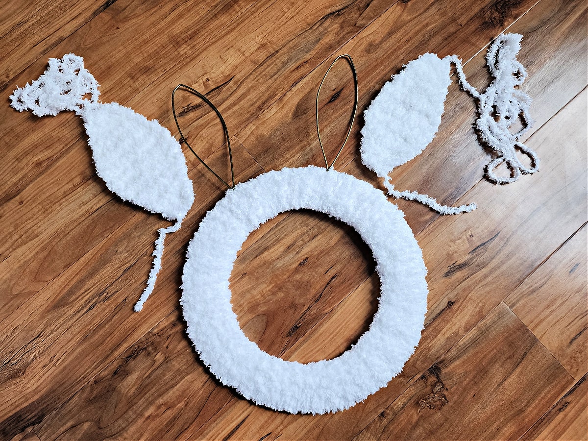 Two crochet bunny ears laying next to bunny wreath form.