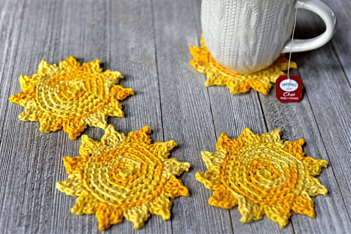 Bright yellow sun shaped crochet coasters with coffee mug.