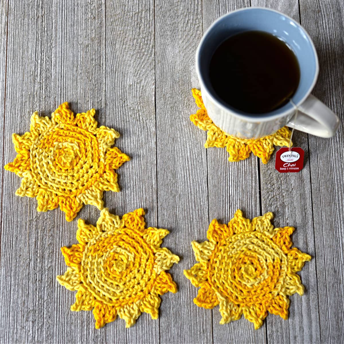 Four yellow sun shaped crochet coasters with coffee mug.