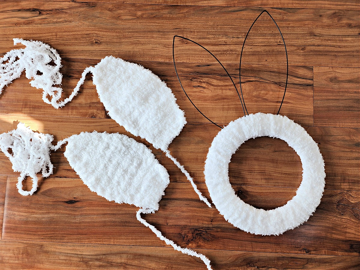 Crochet bunny ears and bunny wreath form laying on wood surface.