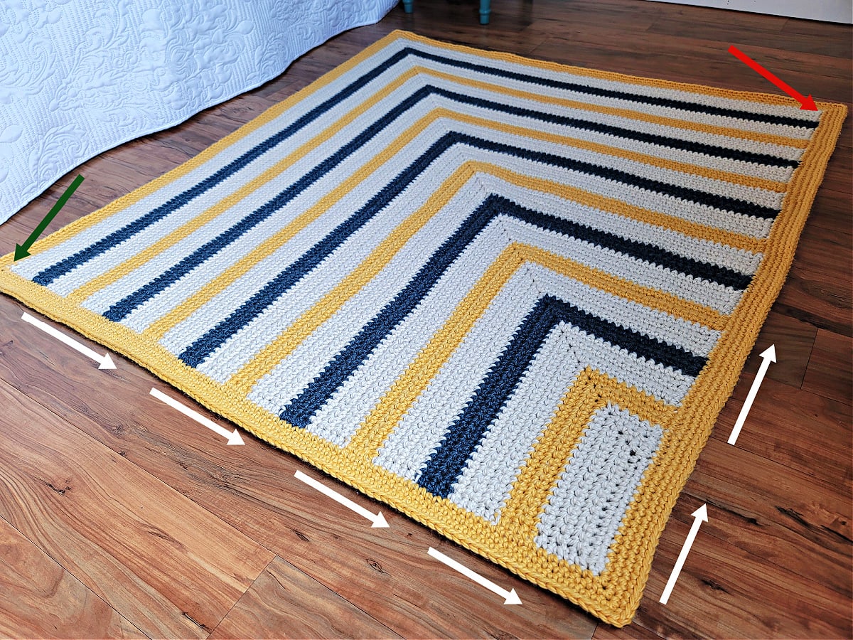 A photo of a 3 color striped crochet blanket with arrows showing the direction to crochet a border.